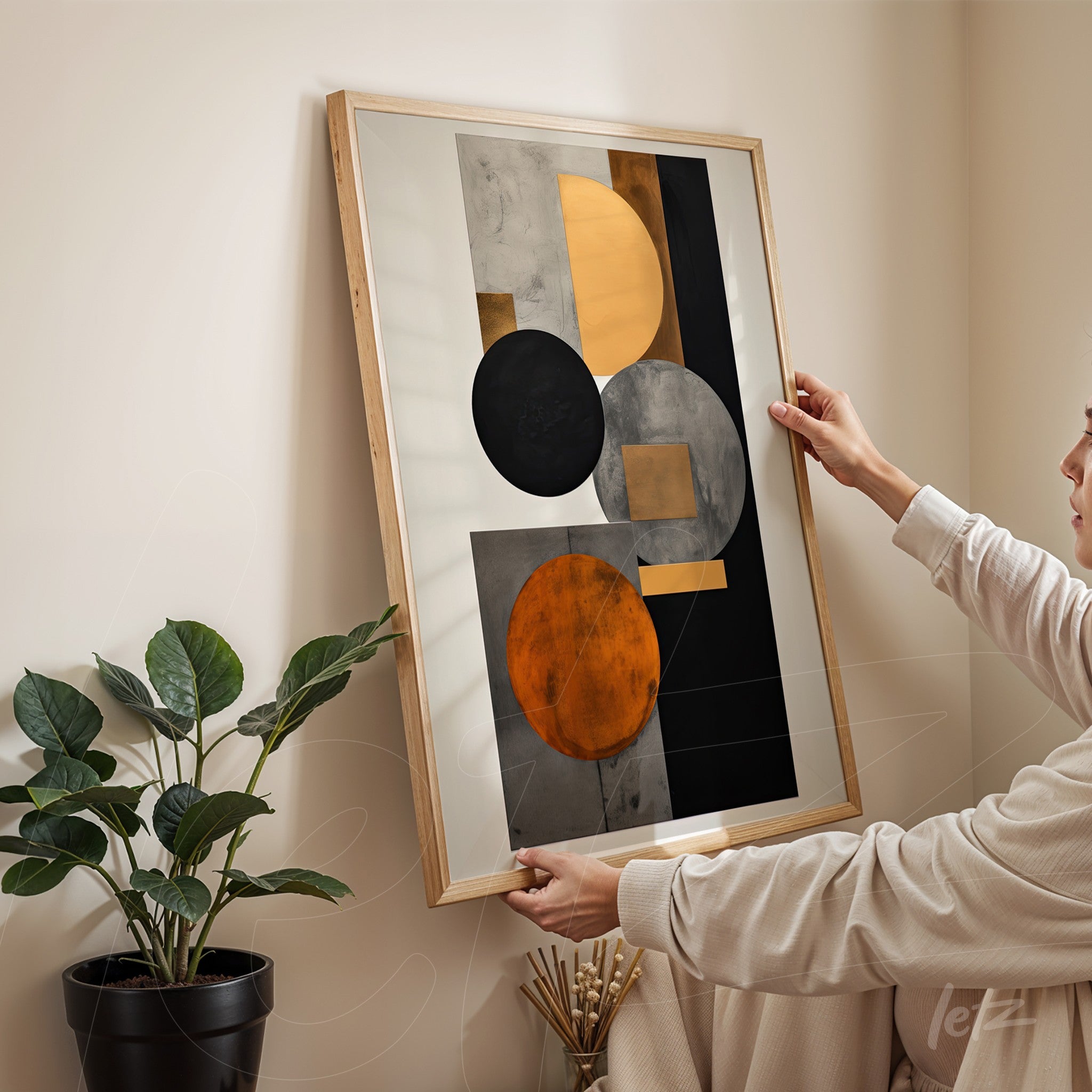abstract wall art featuring black, orange, and gray tones in light wood frame with a woman holding it against a neutral wall
