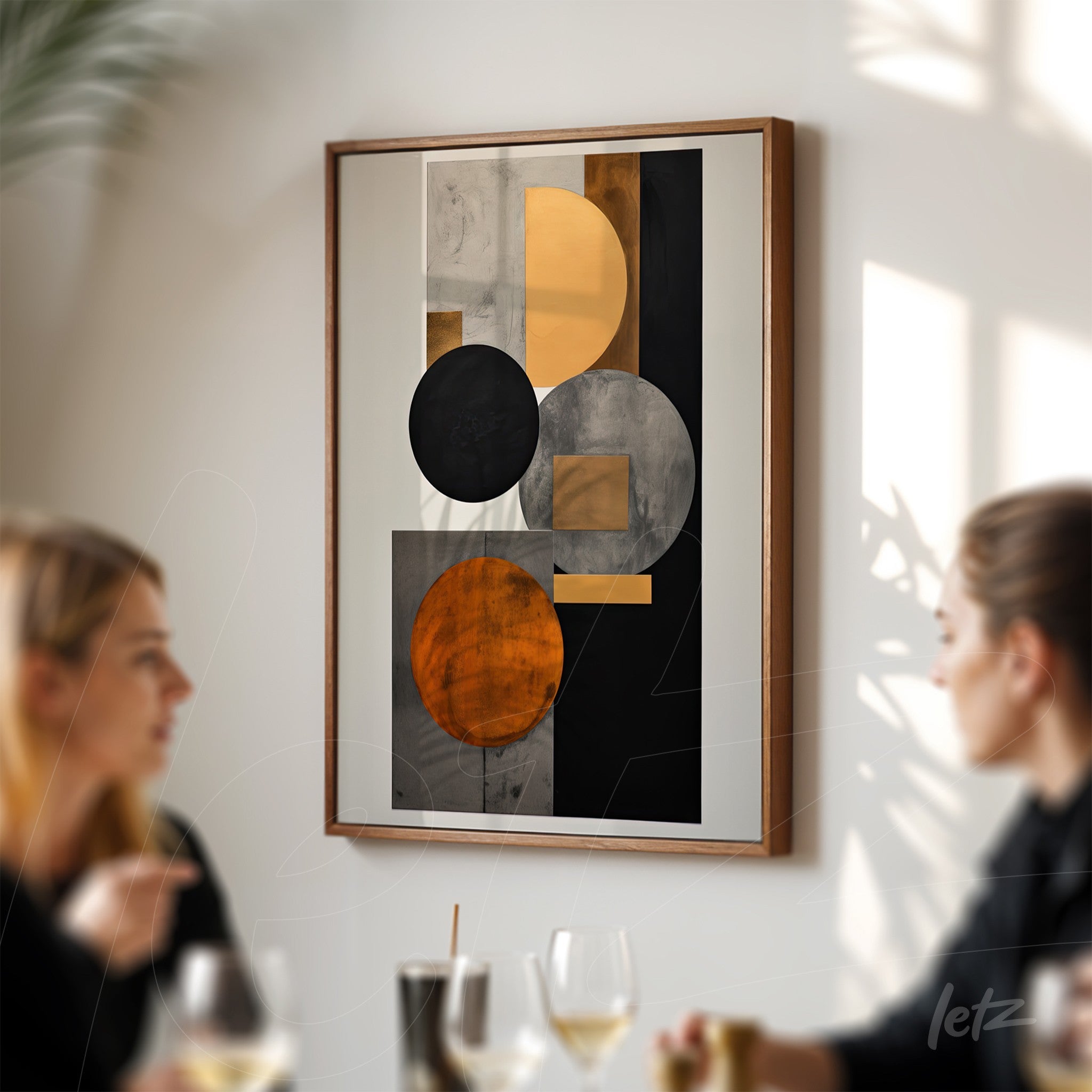 abstract wall art in black, gray, and gold tones displayed in a light wood frame on a wall