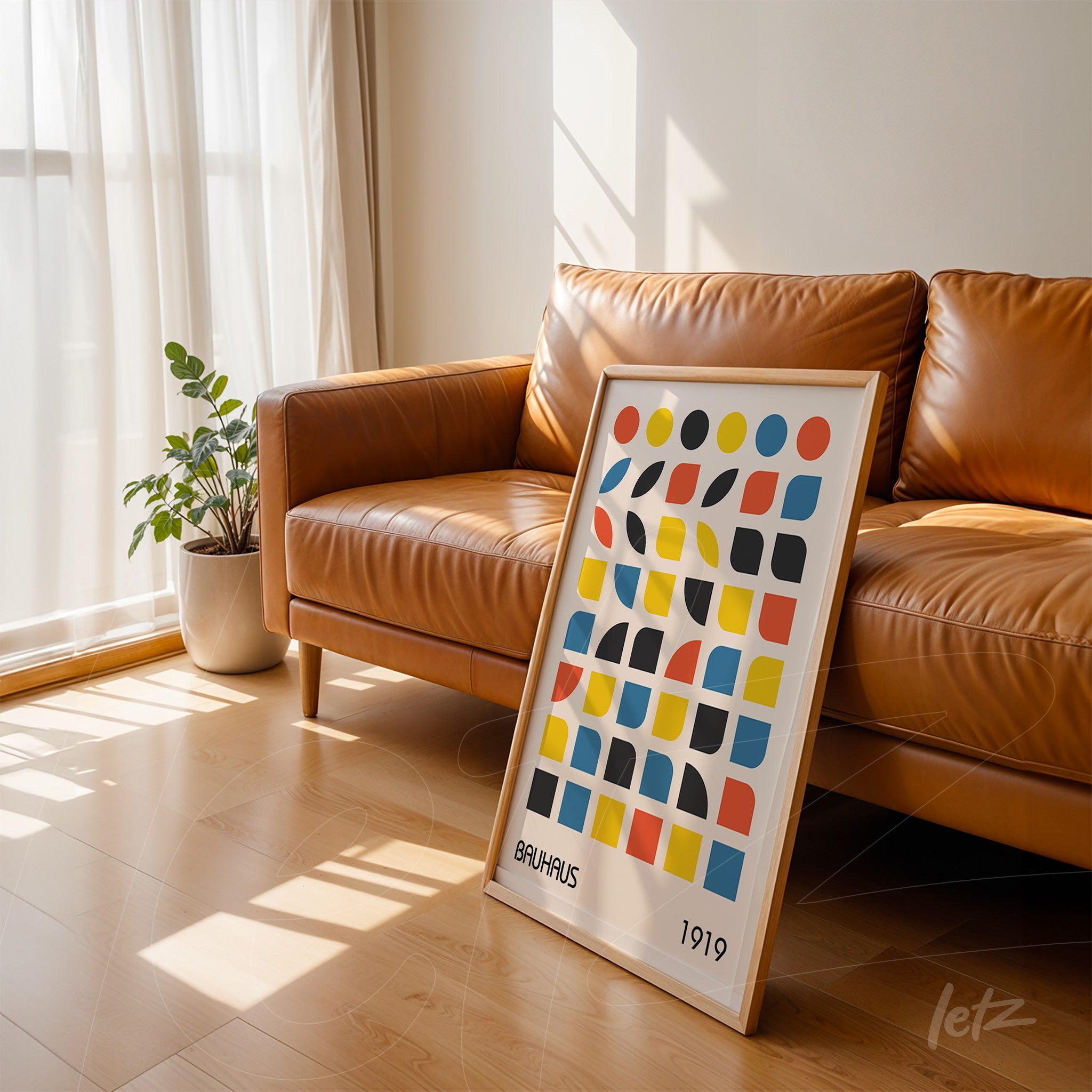 framed wall art leaning on brown leather sofa featuring colorful geometric Bauhaus design with light frame