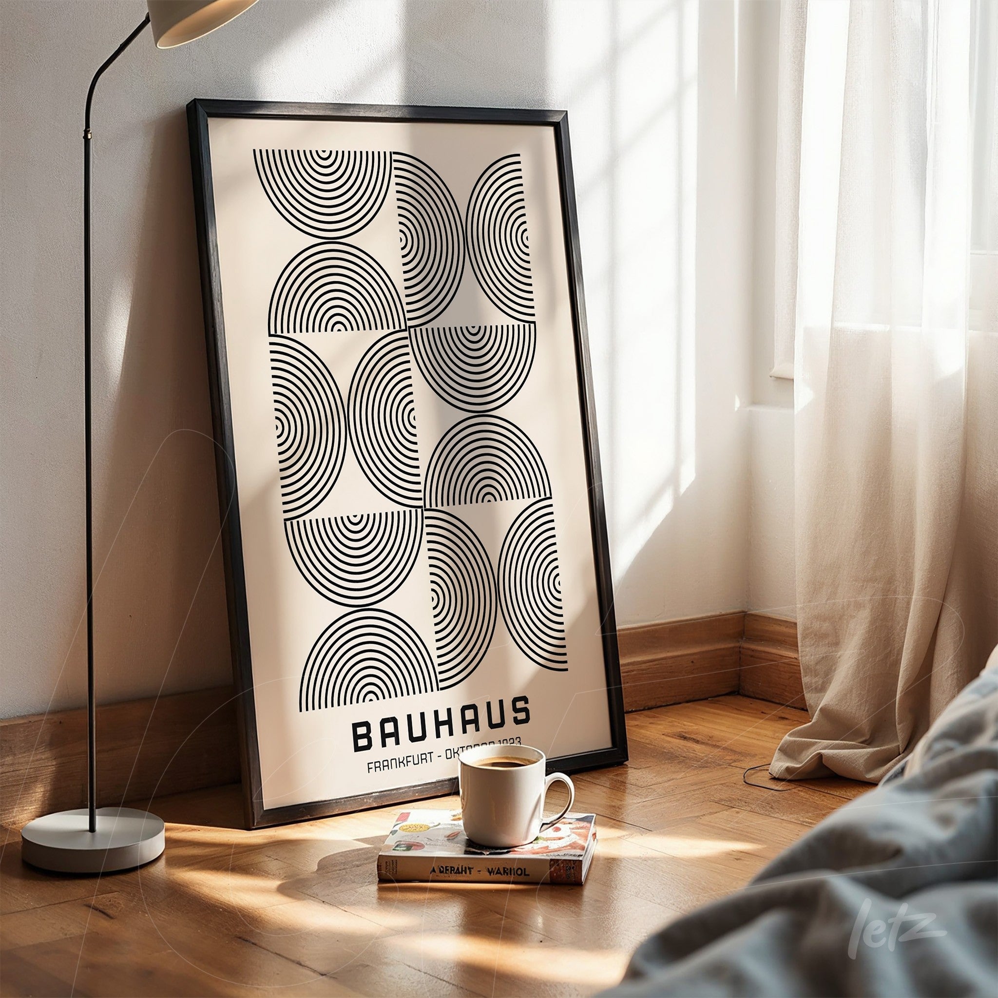 printed poster of geometric bauhaus style art with black frame, propped on wooden floor next to modern lamp