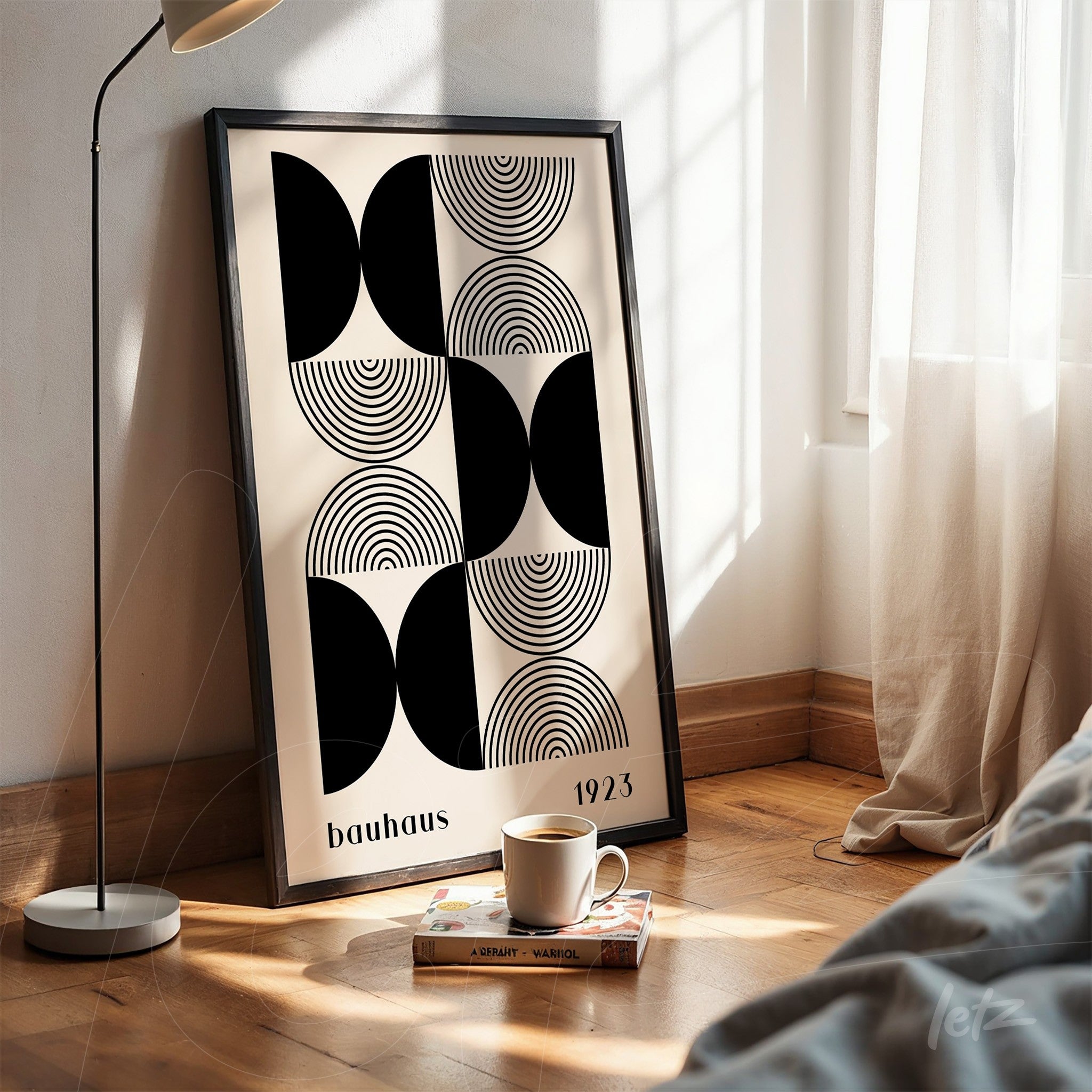 poster with Bauhaus style geometric art in black frame, resting on the floor next to a modern lamp