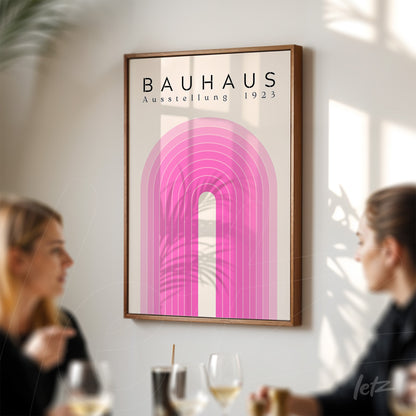 framed poster with futuristic geometric design in pink hues and text 'bauhaus ausstellung 1923', displayed on a light wall