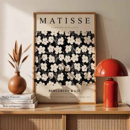 framed artwork featuring black and white floral and plant illustrations in the style of Matisse displayed on a light wall with decorative elements around it