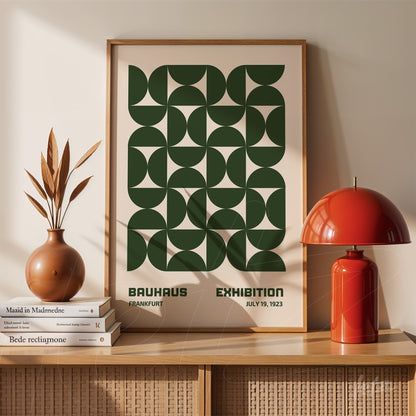 poster print featuring a green geometric bauhaus design displayed on a wooden shelf with a vase and red lamp beside it