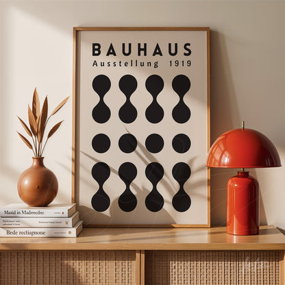 poster print featuring modern design of black geometric shapes on beige background with 'Bauhaus Ausstellung 1919' text, framed and placed on light wooden sideboard next to a red lamp