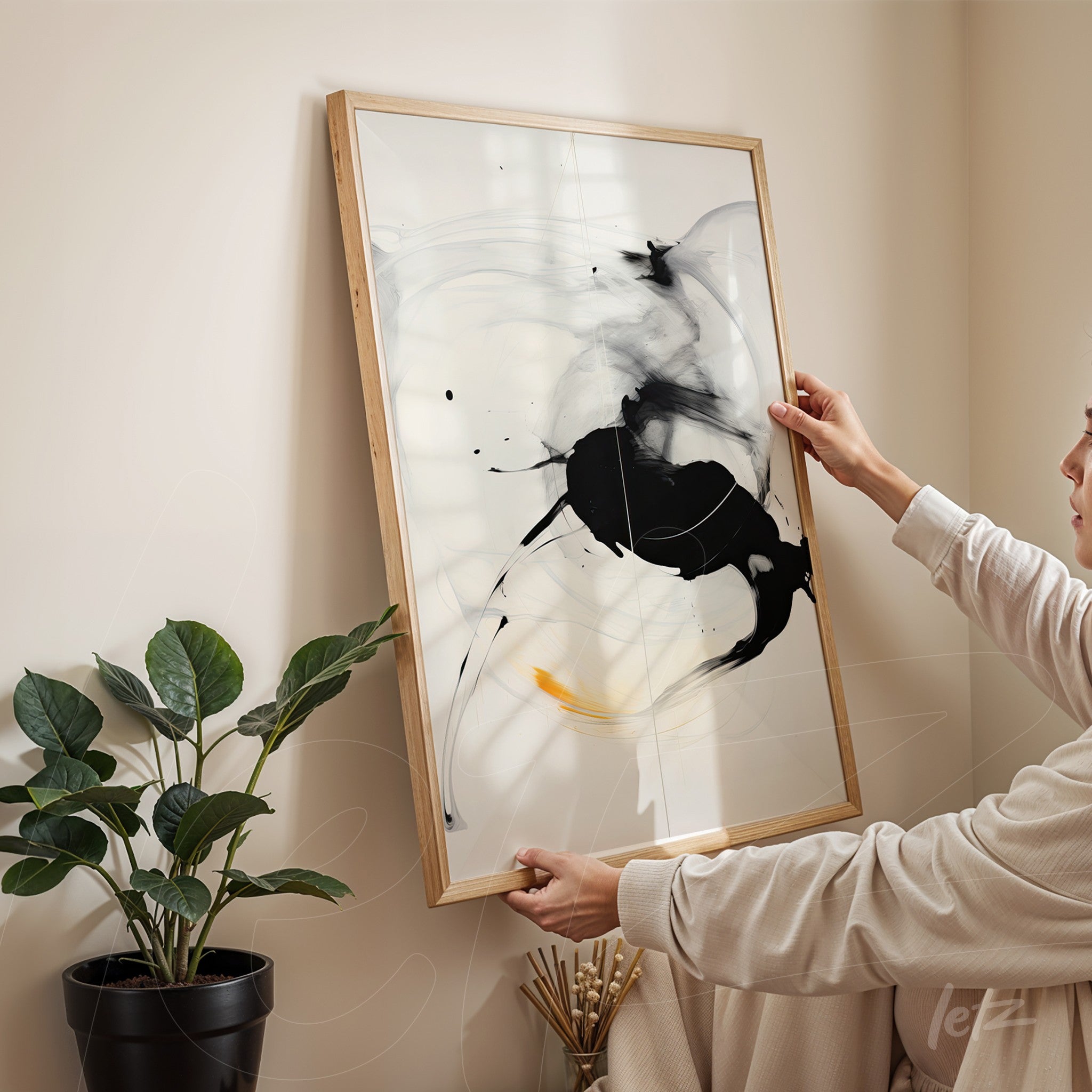 framed abstract art in black and white with light wood frame held by a person in a cozy setting