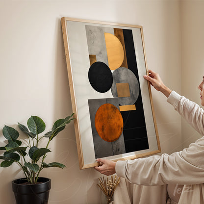 abstract wall art featuring black, orange, and gray tones in light wood frame with a woman holding it against a neutral wall