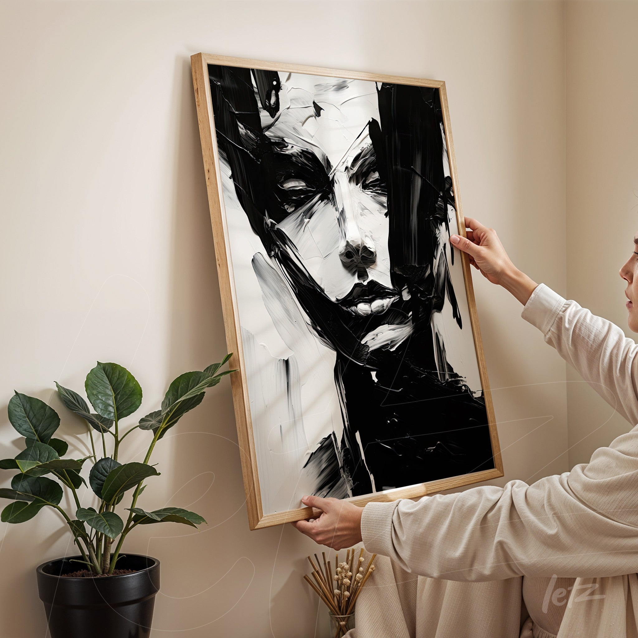abstract artwork in black and white featuring a human figure in a natural wood frame displayed in a minimalist setting with a plant in the background