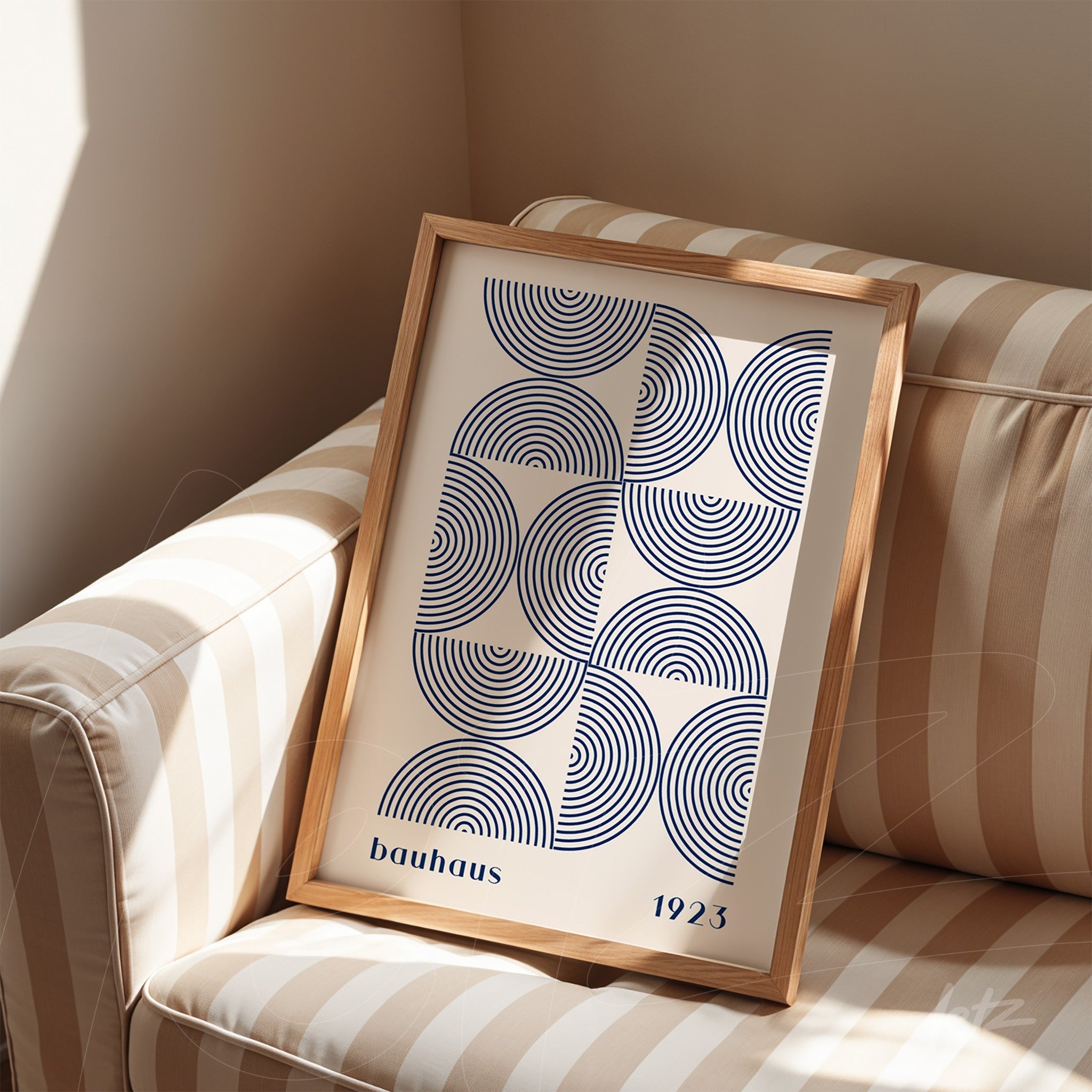 printed poster displayed on striped sofa featuring blue geometric design on white background in a light wood frame
