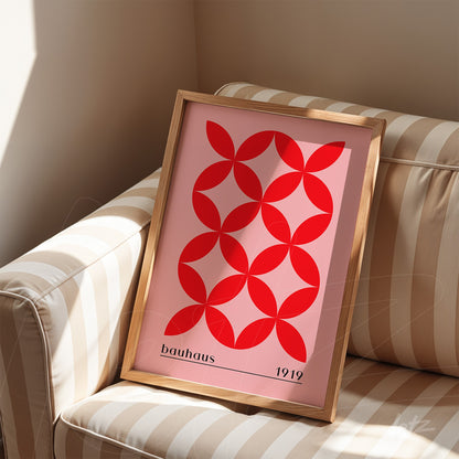 poster print with Bauhaus style geometric design of red circles on pink background in natural wood frame, placed on a striped sofa