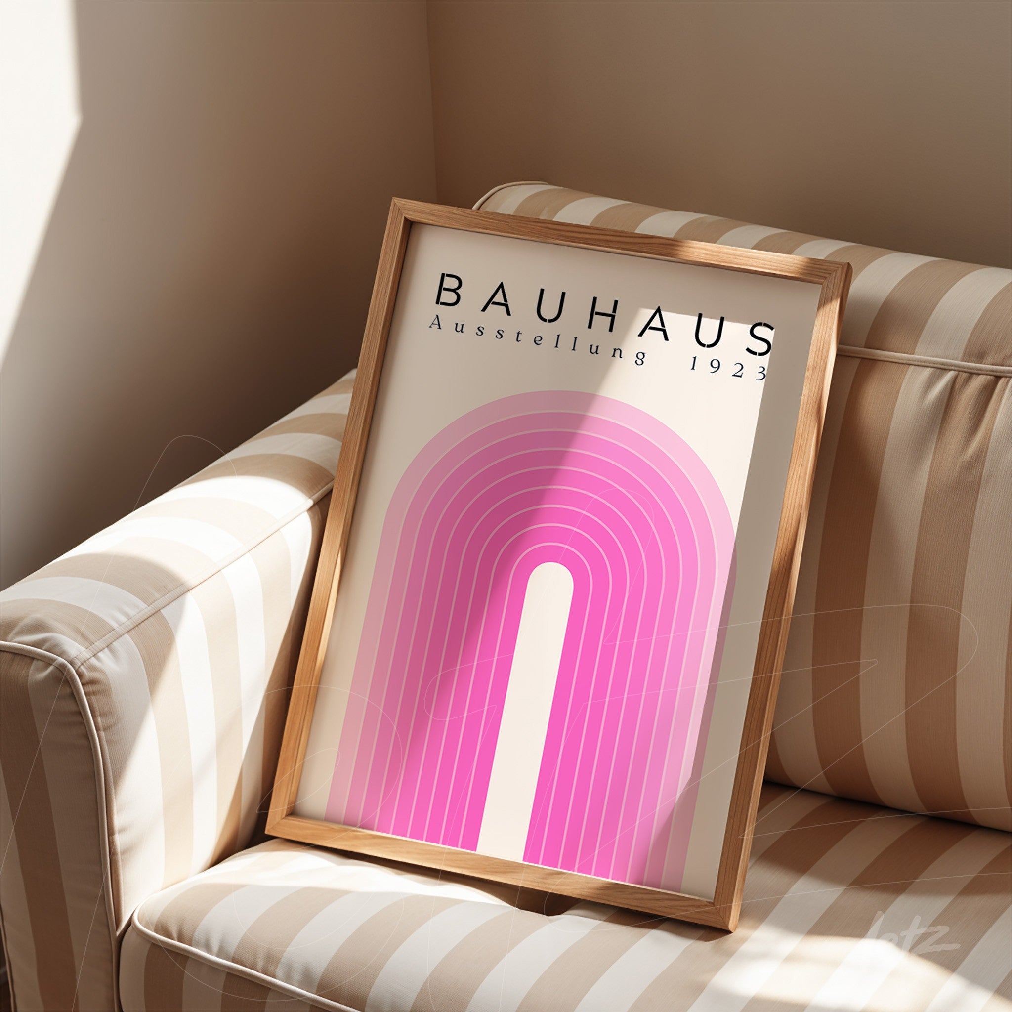 framed art piece with minimalist Bauhaus design in pink tones resting on a striped sofa with light wood frame