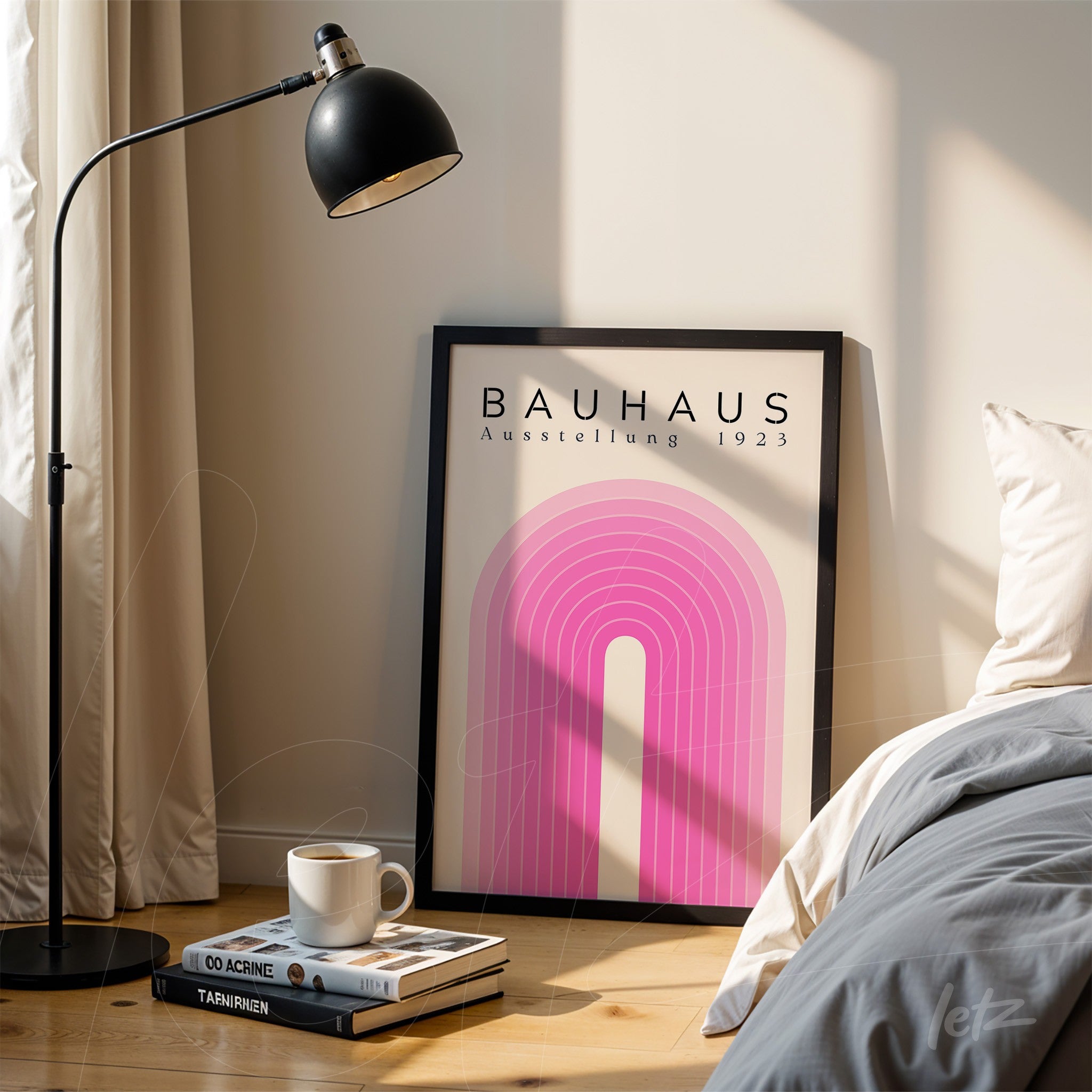 image of a poster with pink geometric design in a black frame, leaning on the floor next to a lamp and a book