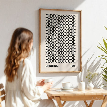 framed artwork with black geometric pattern and 'bauhaus 1919' text in light wood frame displayed on white wall next to plant
