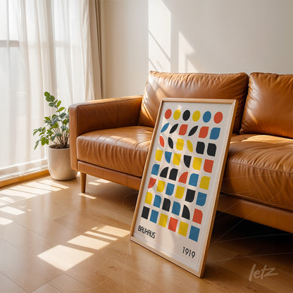 framed wall art leaning on brown leather sofa featuring colorful geometric Bauhaus design with light frame