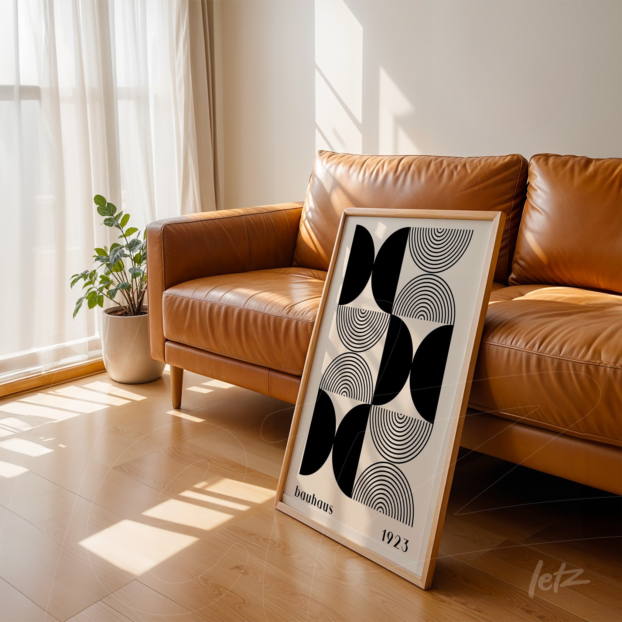 modern geometric black and white art leaning against a brown leather sofa on light wood flooring