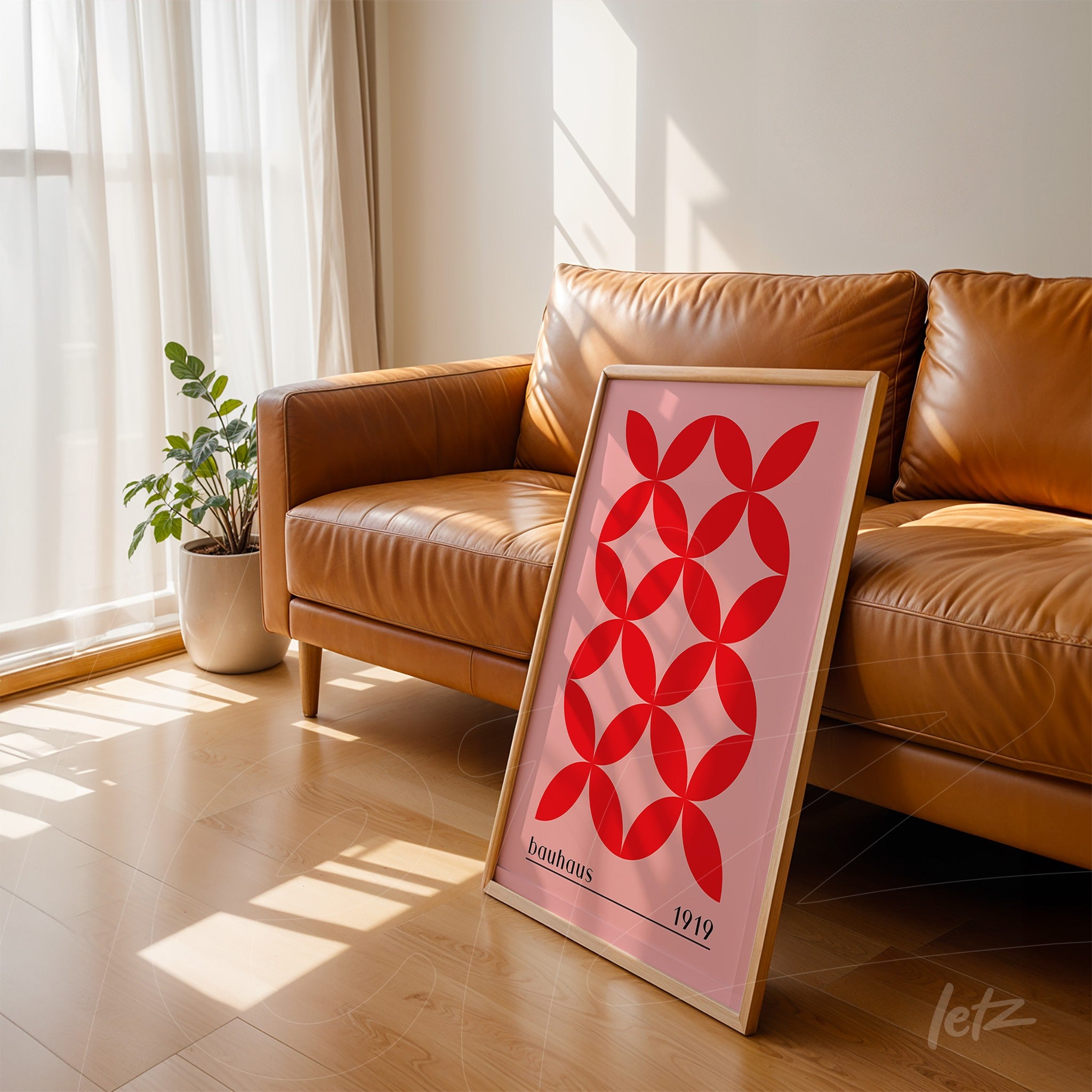modern art with red geometric pattern on pink background framed in light wood leaning against a leather couch