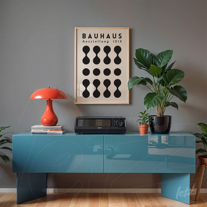 black and white geometric design poster in light frame displayed on gray wall, accompanied by plants and red lamp