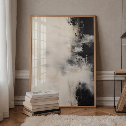abstract art piece in light and dark tones in a light wood frame leaning against a table next to stacked books