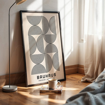 printed poster of geometric bauhaus style art with black frame, propped on wooden floor next to modern lamp