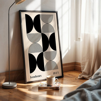 poster with Bauhaus style geometric art in black frame, resting on the floor next to a modern lamp