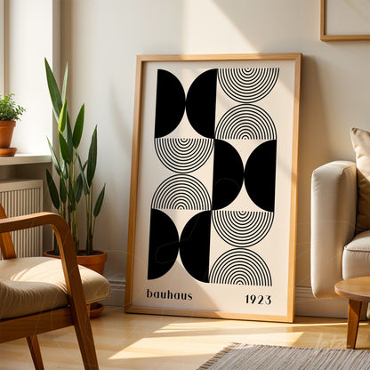 poster print featuring black and white geometric bauhaus-inspired art with light wood frame, resting on the floor beside a couch in a well-lit living room