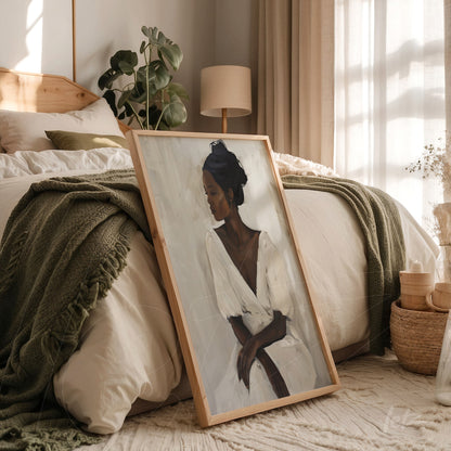 framed art of a woman in neutral tones leaning against a bed with wool blankets and minimalistic decor