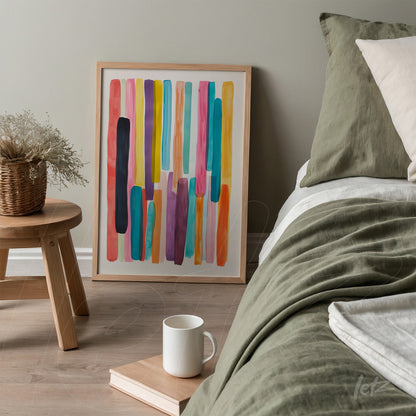 framed abstract art in vibrant colors leaning beside a bed in a cozy setting