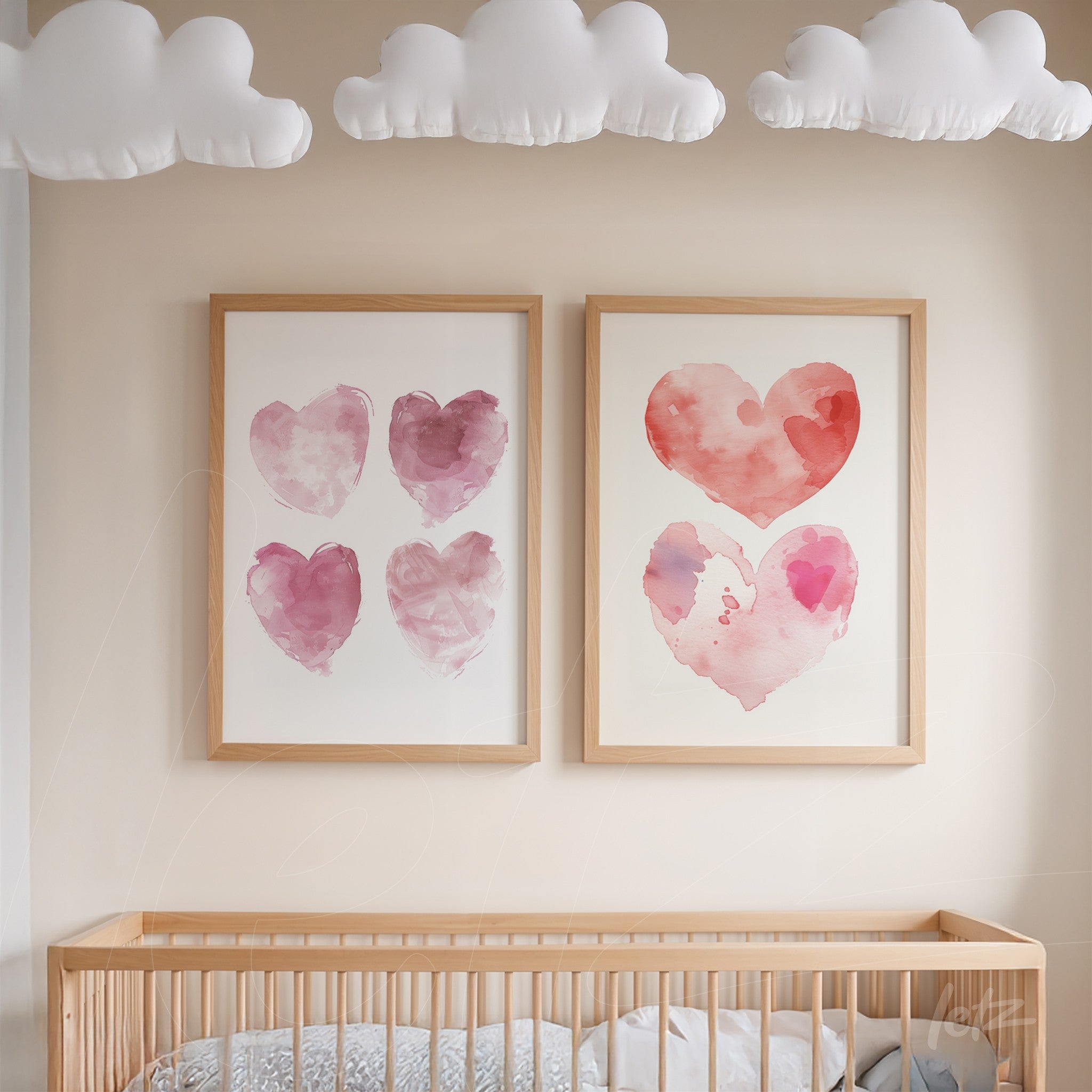 pair of framed watercolor heart illustrations in pink hues with light wood frames displayed above a wooden crib beneath decorative clouds
