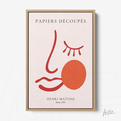 framed modern art print featuring a stylized face in red and pink tones with a light wood frame